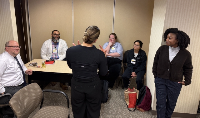OCC Members presenting at UMMC; Group of people talking around a desk in a brown room 