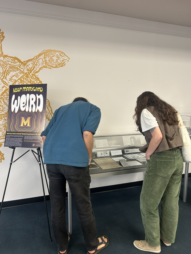 Visitors looking into a glass box of historical artifacts at Keep Maryland Weird Exhibit
