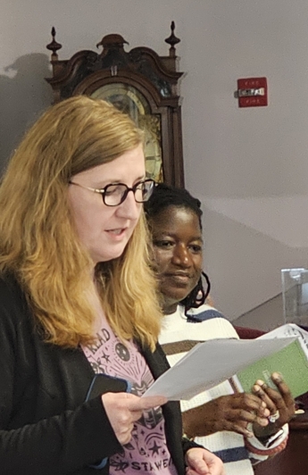 Dr. Carly Woods and Felicity Dogbatse presenting at the Keep Maryland Weird Exhibit, reading from a piece of paper in a pink shirt 